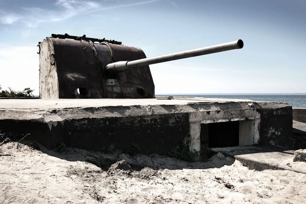 A weathered concrete coastal artillery emplacement sits isolated on the sand. The long gun barrel points out toward the ocean horizon.
