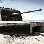 Toruń A weathered concrete coastal artillery emplacement sits isolated on the sand. The long gun barrel points out toward the ocean horizon.