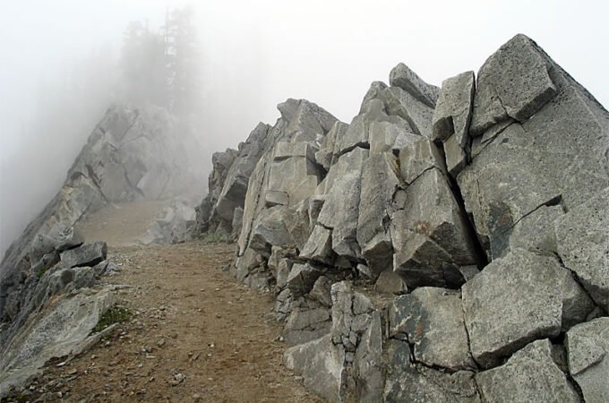 A misty mountain trail winds through jagged rocks, creating a mysterious and serene atmosphere.