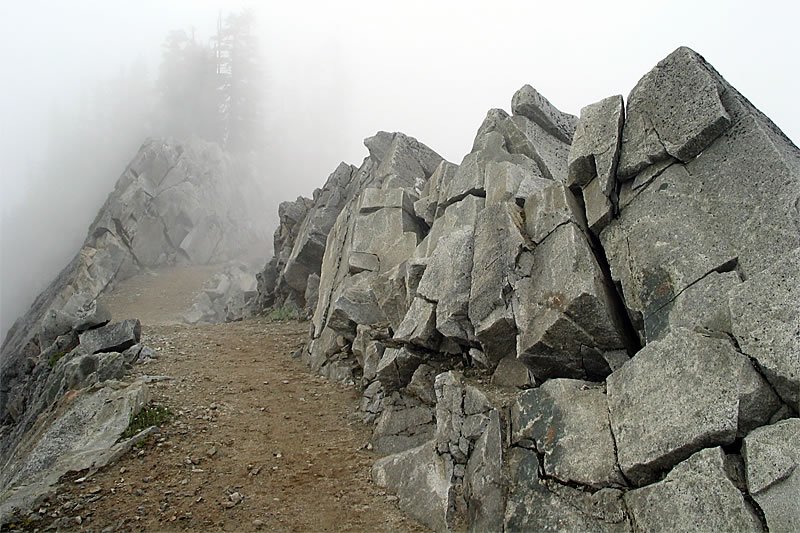 A misty mountain trail winds through jagged rocks, creating a mysterious and serene atmosphere.