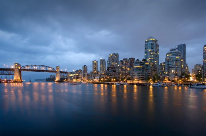 City skyline at dusk with a bridge and lights reflecting on water.