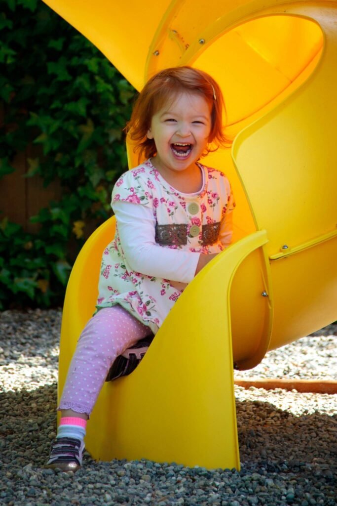 Children playing together. Bright smiles on bright yellow slides.