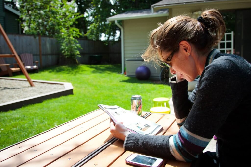 Relaxing with a magazine on a shaded wooden picnic table in a green backyard. A peaceful Seattle garden scene with a private entrance and cozy outdoor seating.