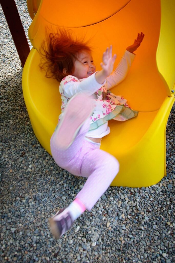 A child laughing joyfully as they slide down a vibrant orange and yellow playground slide.