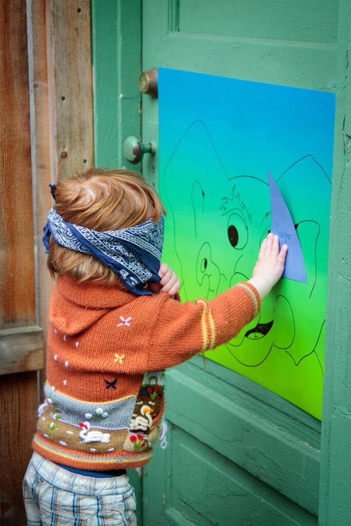 A person wearing a blindfold uses a shape tool to trace an outline on a green paper attached to a teal door, engaging in a sensory art activity.