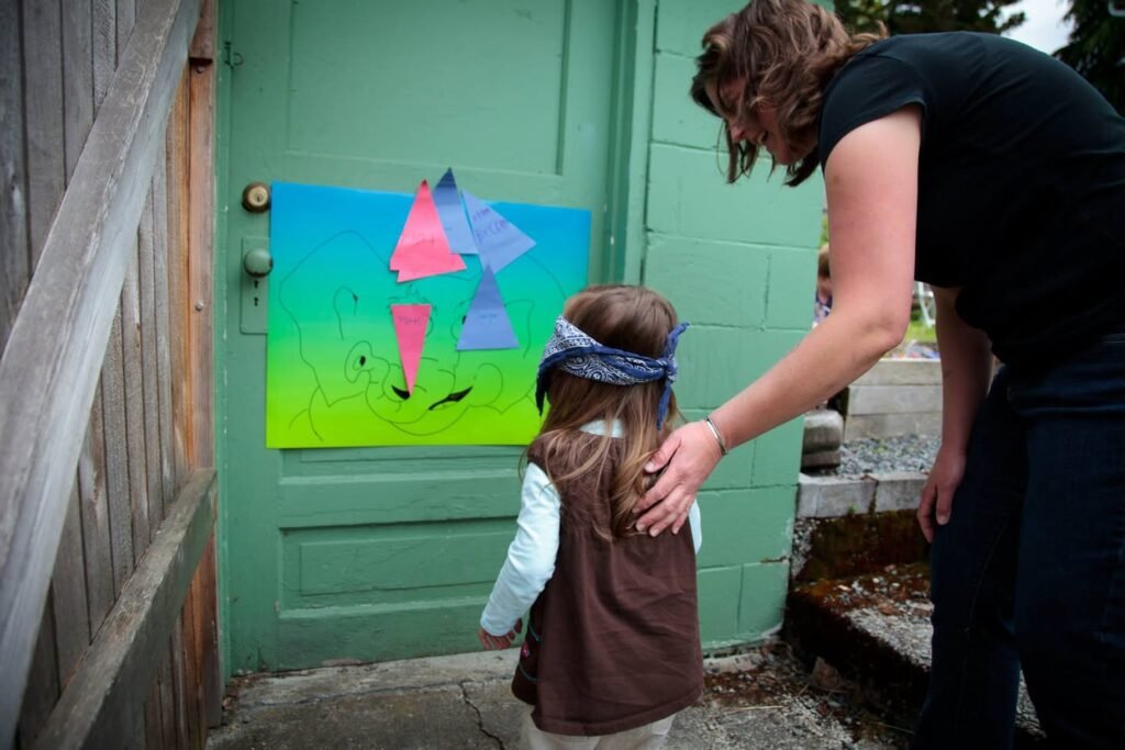 A child stands before a colorful geometric painting on a green door as a person places a hand gently on their back.