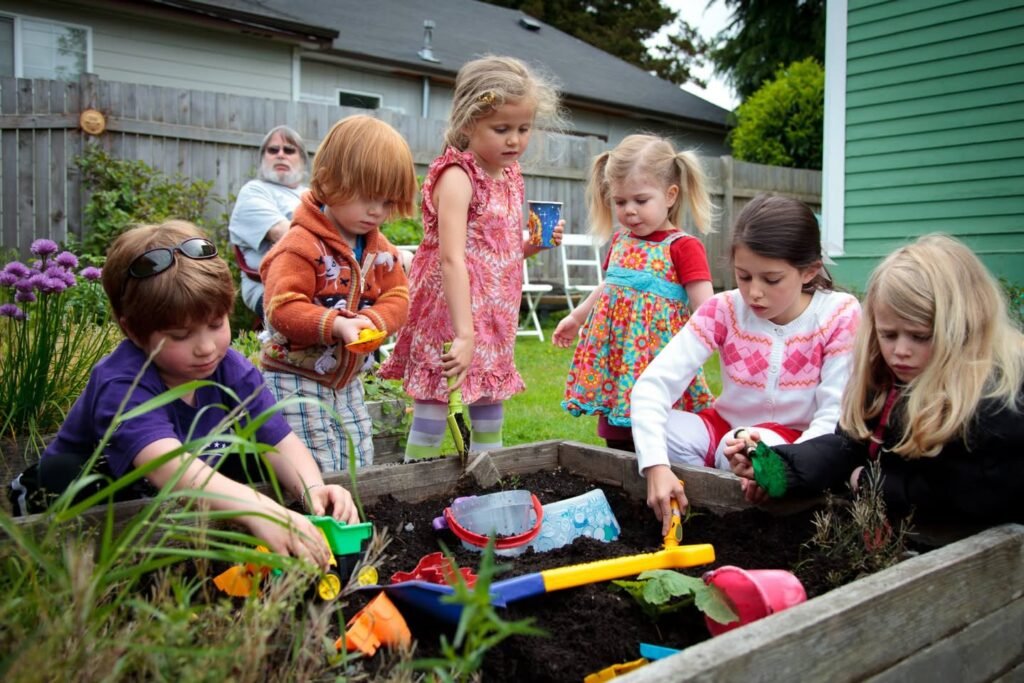 Children playing with colorful toys in a plant tray in a garden and a woman in the background.