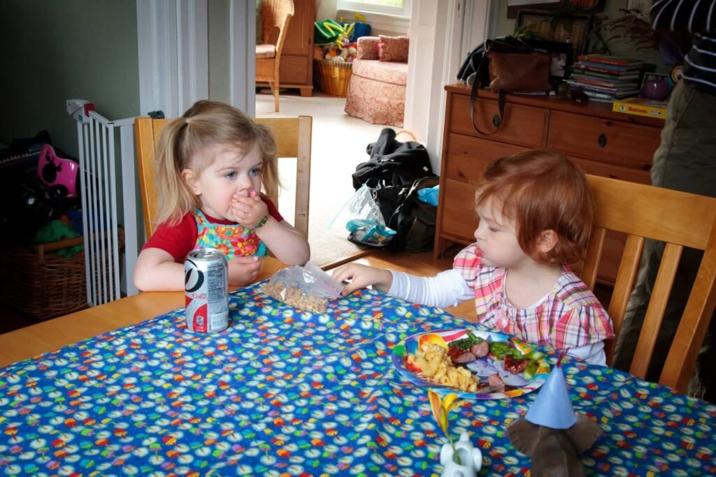 Two young children enjoying a meal at a wooden dining table with a colorful tablecloth in a cozy home setting.