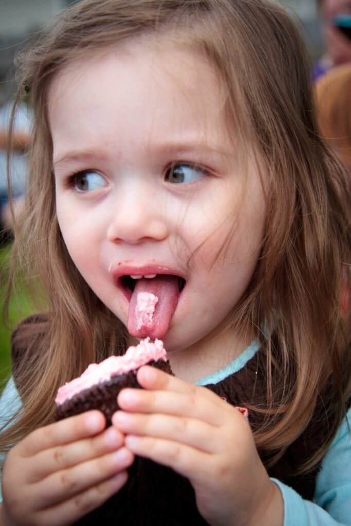 A close-up of a child extending their tongue to lick a pink-frosted chocolate ice cream bar.