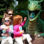 A family enjoys a sunny day visiting a dragon statue at an outdoor attraction.