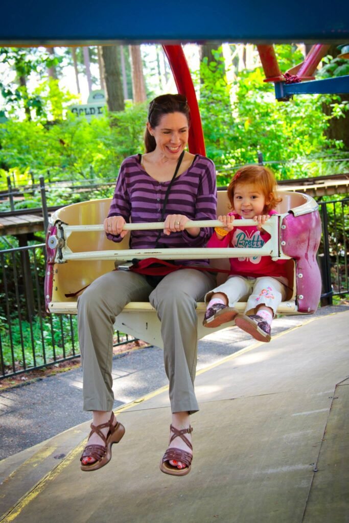 A person and child enjoy a swing ride at an amusement park surrounded by trees.