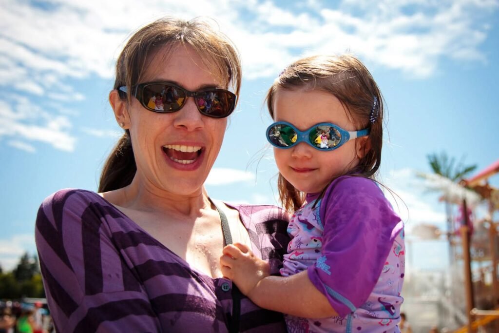 A joyful moment during a sunny day outdoors featuring two people wearing sunglasses and purple tops.