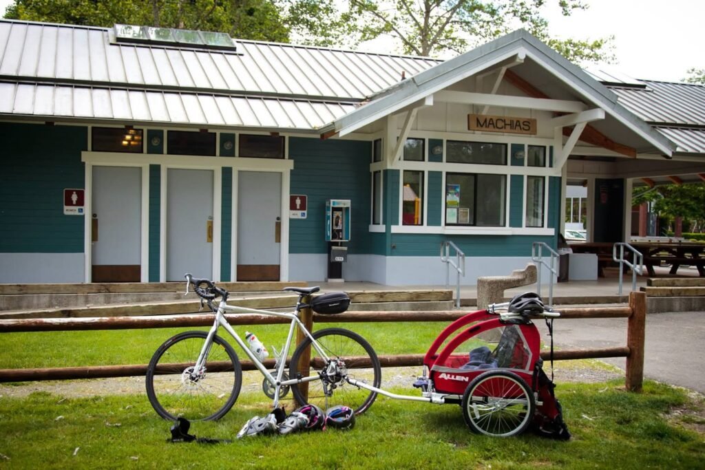 A bicycle and red stroller parked on grass in front of a scenic PNW building.