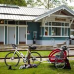 A bicycle and red stroller parked on grass in front of a scenic PNW building.