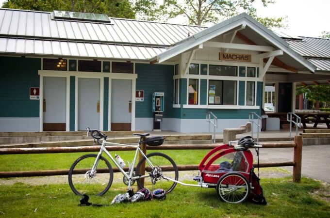 A bicycle and red stroller parked on grass in front of a scenic PNW building.