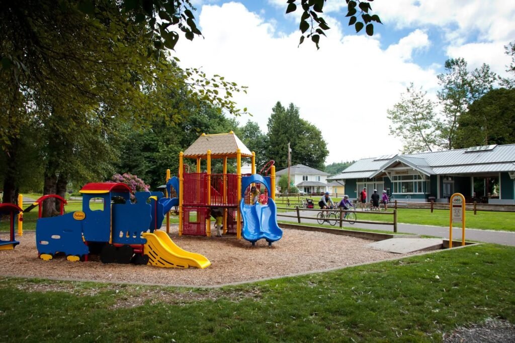 A colorful children's playground featuring a train and slide, surrounded by lush greenery.
