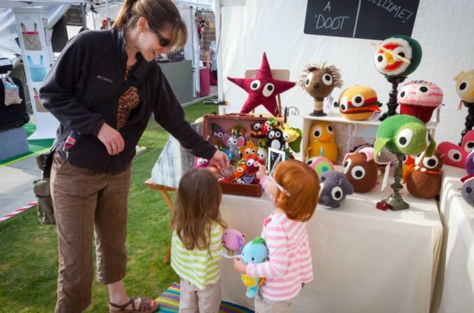A family explores colorful handcrafted plush toys at an outdoor market.