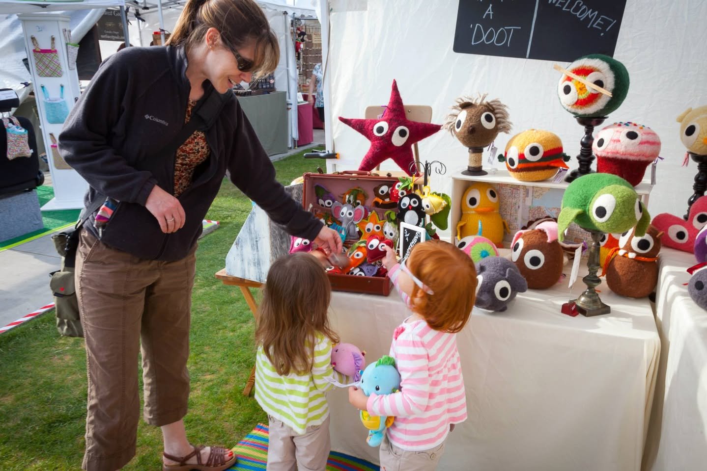 Edmonds Arts Festival A family explores colorful handcrafted plush toys at an outdoor market.