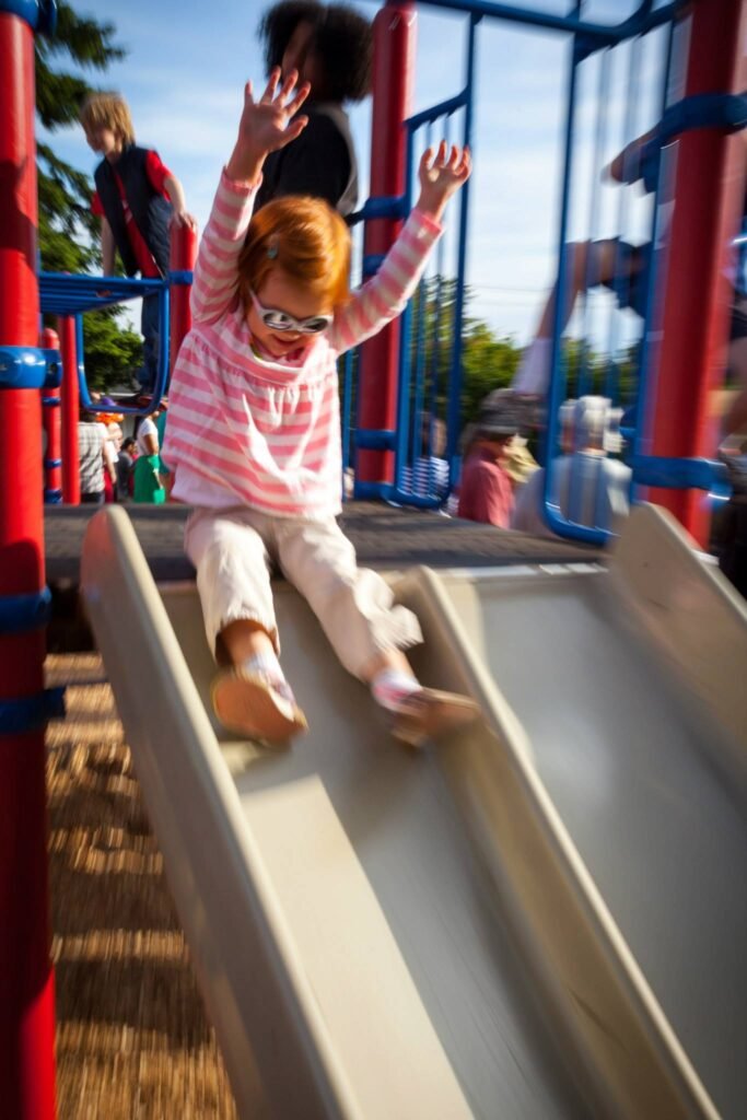 A child slides down a playground slide under a clear sky, conveying a sense of playful energy.