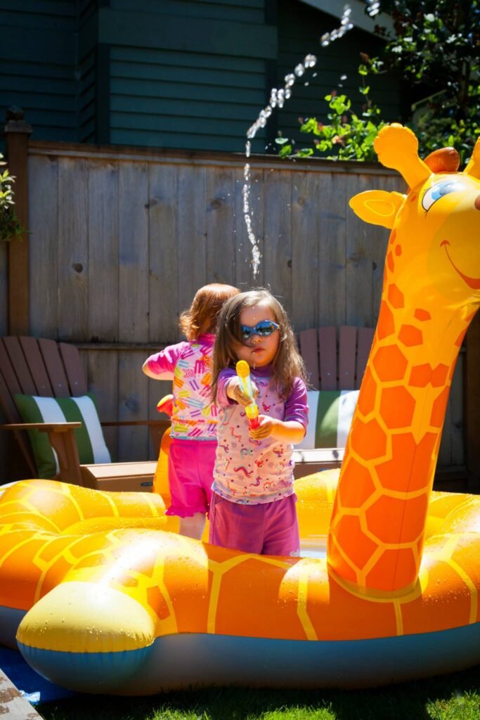 Two children playing in a giraffe-shaped inflatable pool with a fountain in the garden