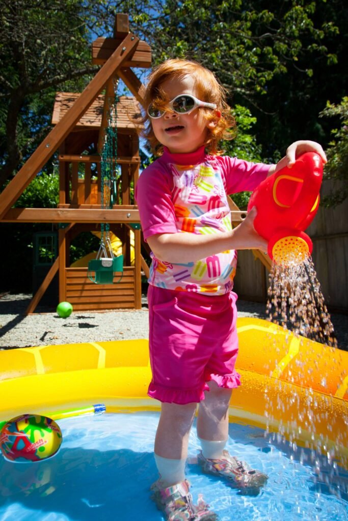 A child playing with water in a backyard kiddie pool near a wooden treehouse.