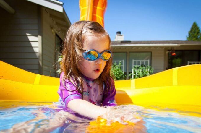 Toddler in colorful goggles plays in a bright yellow bubble pool outdoors.