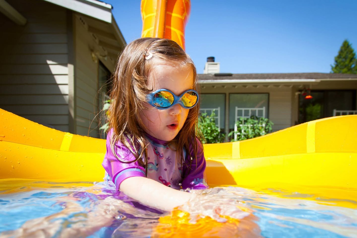 Splish Splash Toddler in colorful goggles plays in a bright yellow bubble pool outdoors.