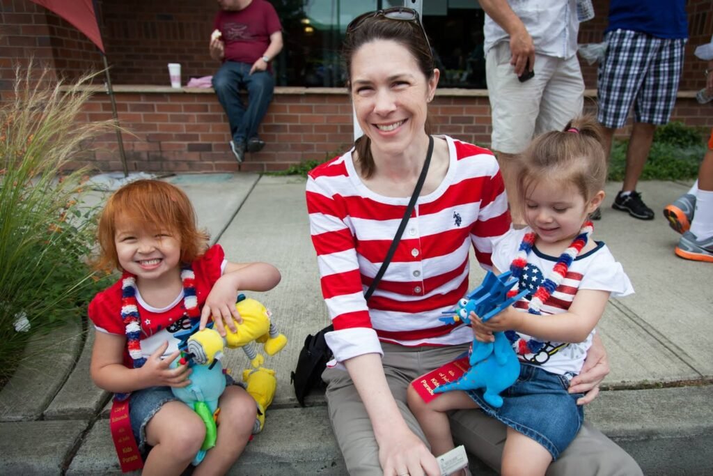 A woman and two children are dressed in red, white, and blue for a July 4th celebration, holding festive toys.