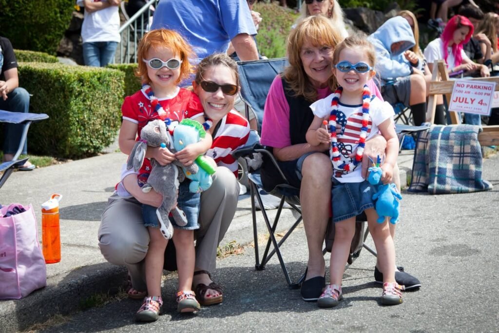 Family members wearing red, white, and blue outfits and holding toy dogs while sitting outdoors at a community event.