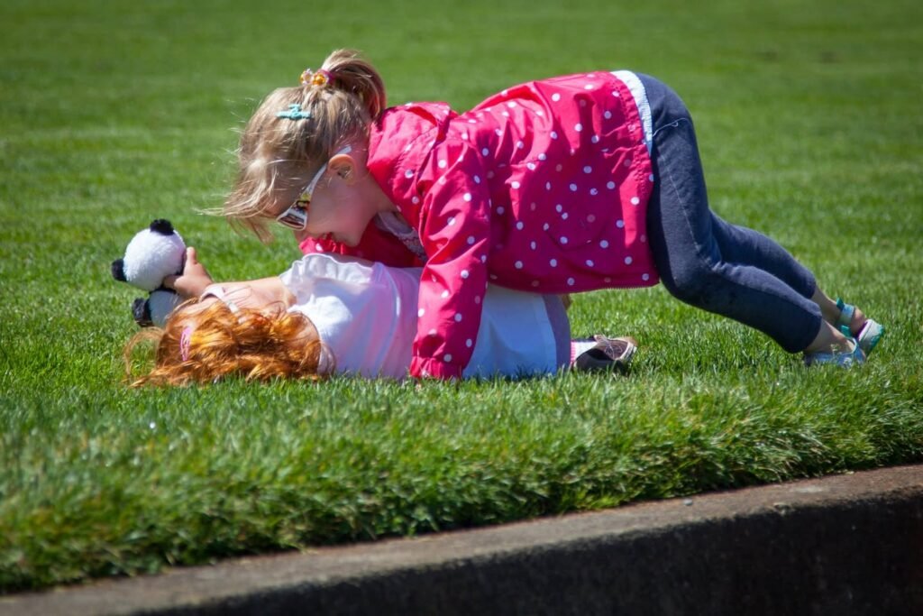 A child in a pink polka-dot jacket playfully poses on the grass with a stuffed panda.