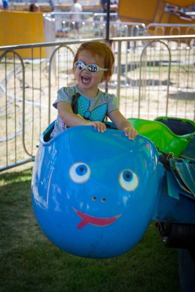 A child enjoying a colorful caterpillar-shaped ride at a fair with a metal fence in the background.