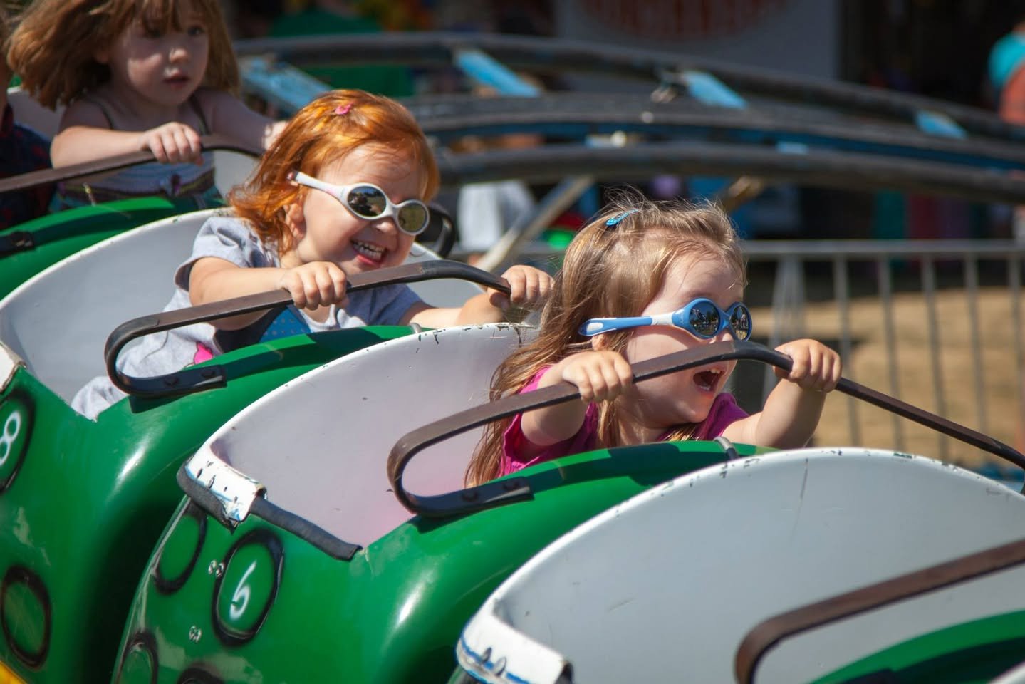 Tour de Terrace Children wearing cool sunglasses enjoy a green roller coaster ride on a sunny day.