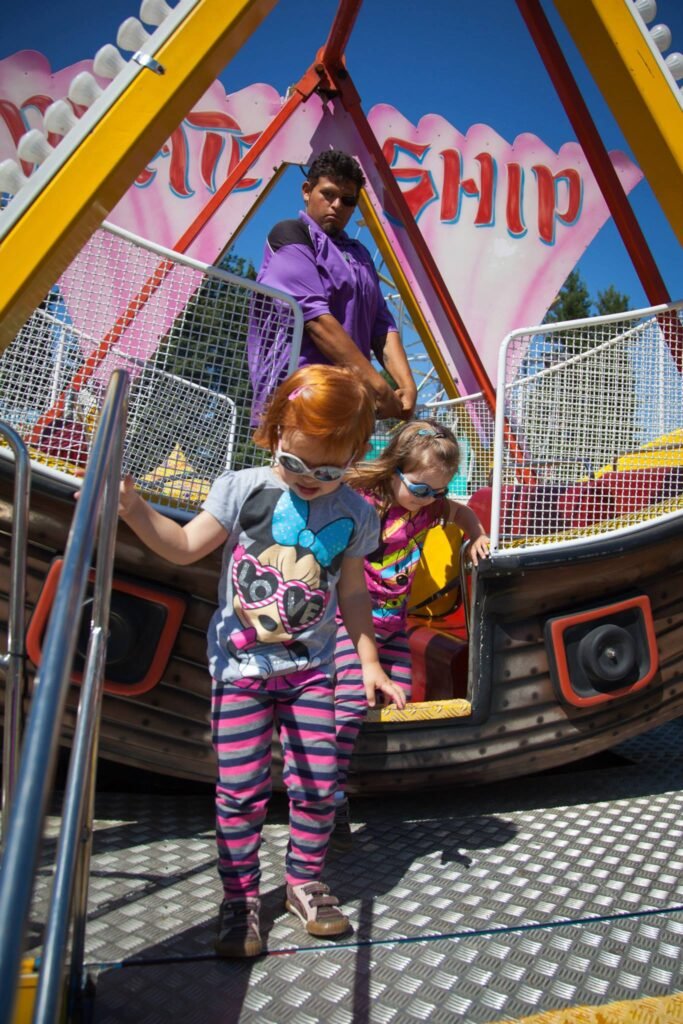 A family enjoys a ship-shaped carnival ride under a bright blue sky with colorful pennant banners.