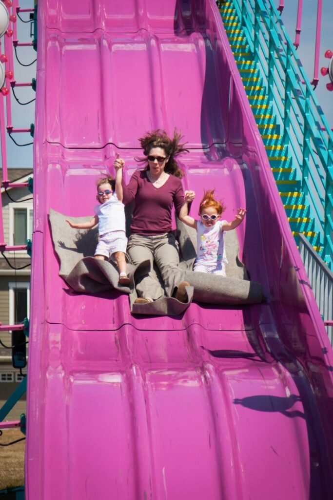 A family sliding down a bright pink inflatable slide at a carnival or fair.