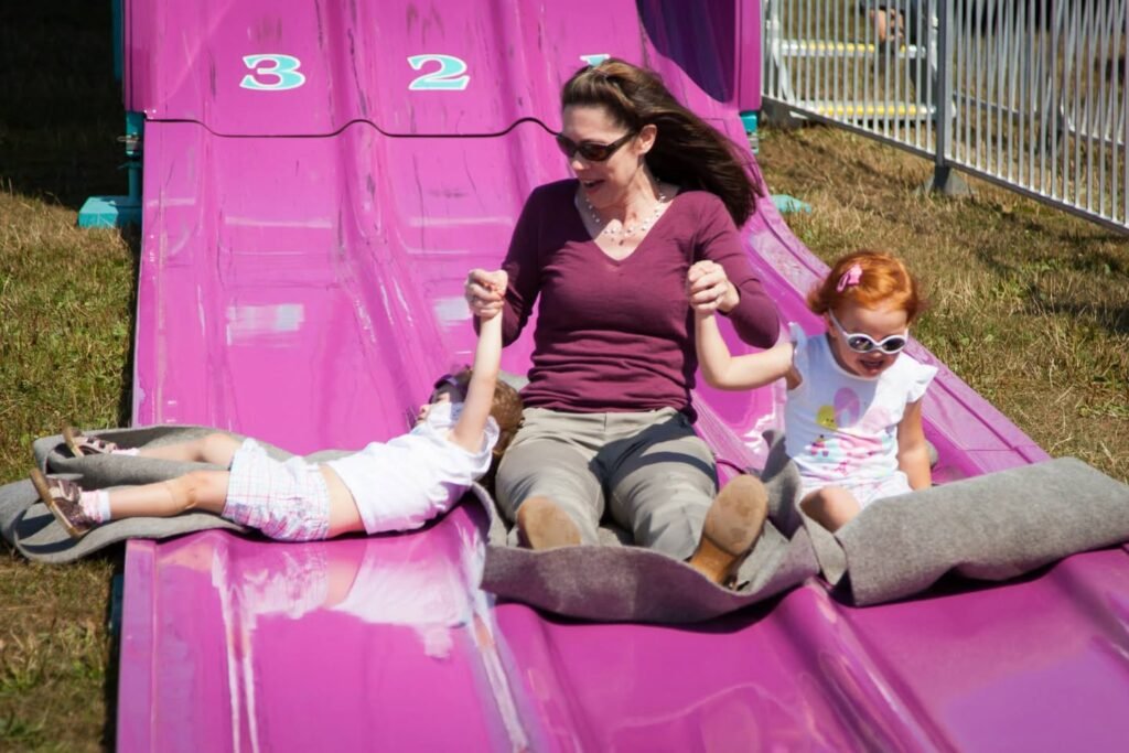 A woman and children enjoying a pink water slide at an outdoor event, with water flowing down the lanes.