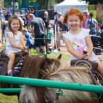Children enjoying a pony ride at a busy outdoor event.
