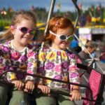 Children enjoying a Ferris ride wearing colorful 3D glasses and funny glasses at a fair.