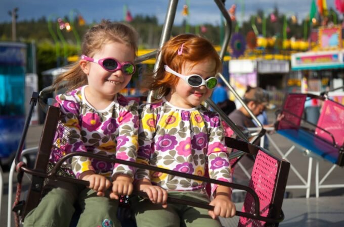 Children enjoying a Ferris ride wearing colorful 3D glasses and funny glasses at a fair.