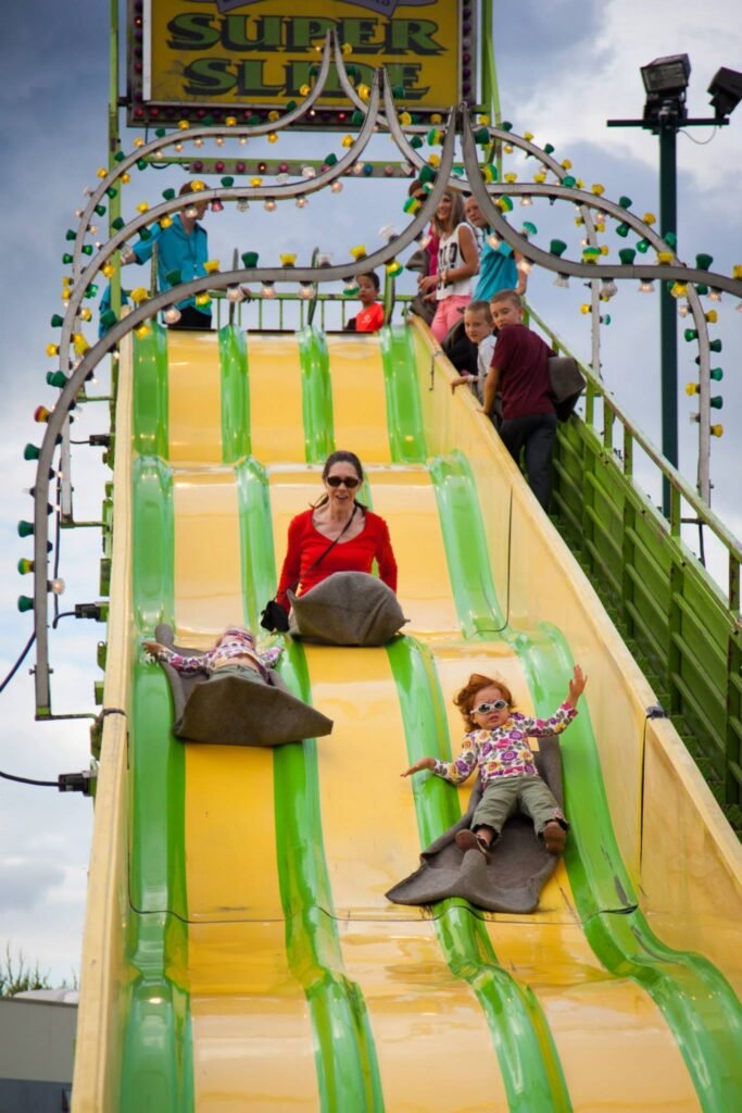 Riders sliding down a bright yellow and green Super Slide attraction at an amusement park.