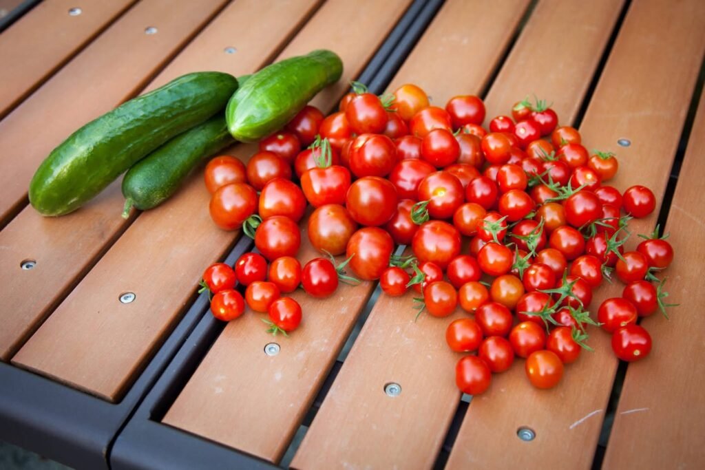 Freshly picked cherry tomatoes and cucumbers arranged on a wooden table. A display of vibrant homegrown vegetables ready to eat.