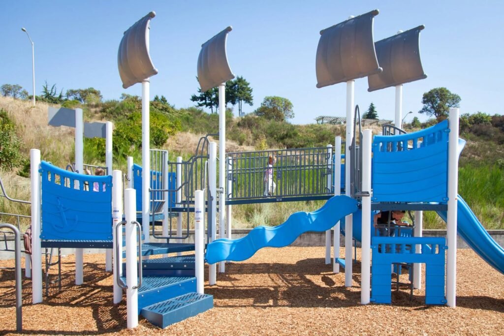 Blue and white playground structure featuring sail-like shade structures in an outdoor park.