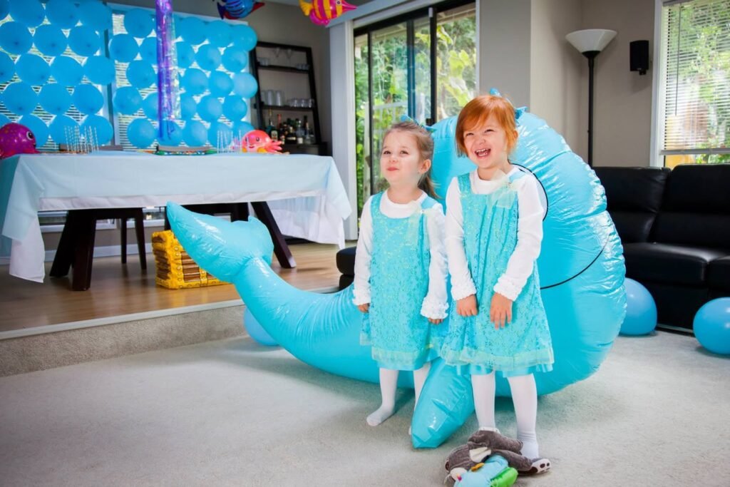 Children in matching outfits posing with a large blue inflatable whale at a bright indoor celebration.
