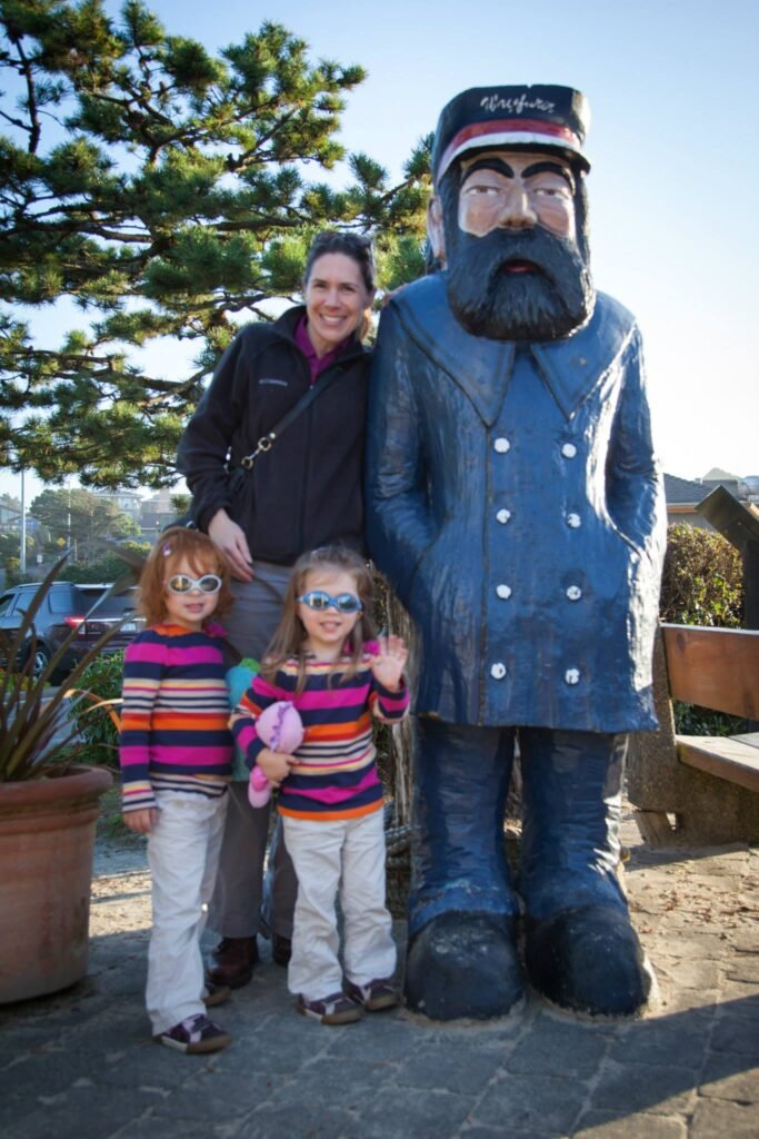 A family poses with a large statue of the Smiling Butcher at a street market, enjoying a sunny day.
