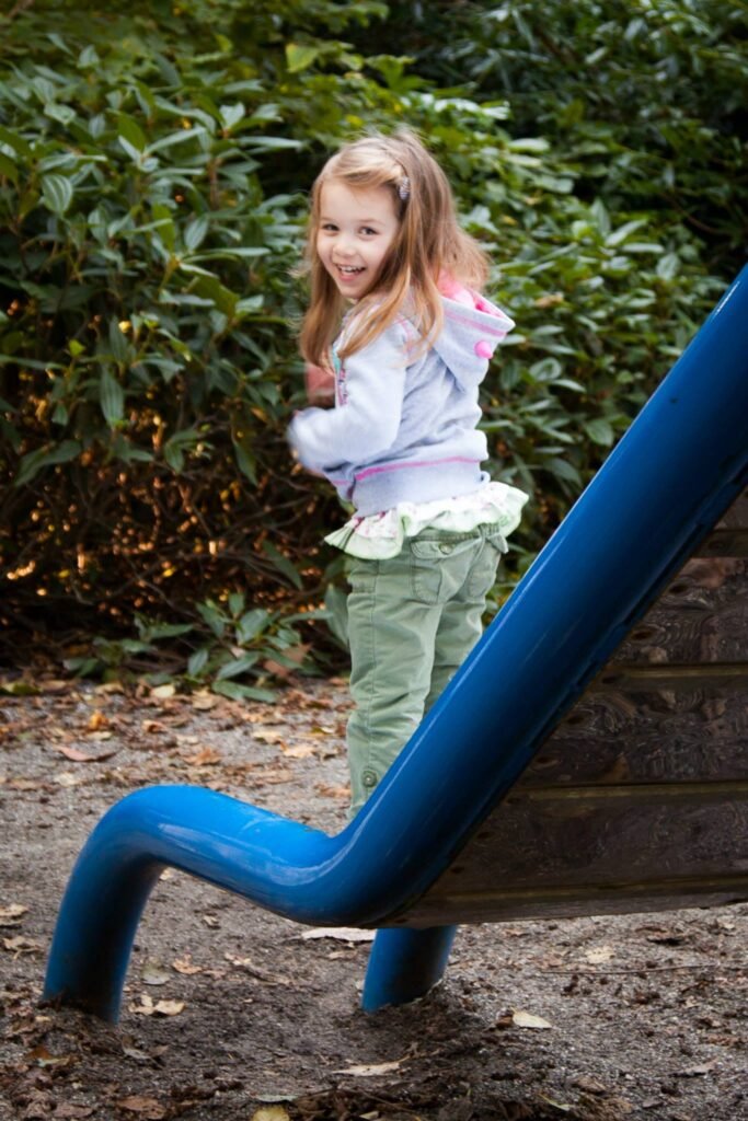 A child playing on a blue playground slide with lush green hedges in the background, capturing a moment of fun outdoors.