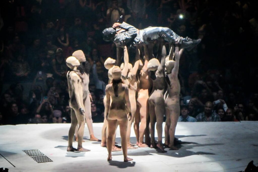 A group of performers in white costumes create a human pyramid on a stage.