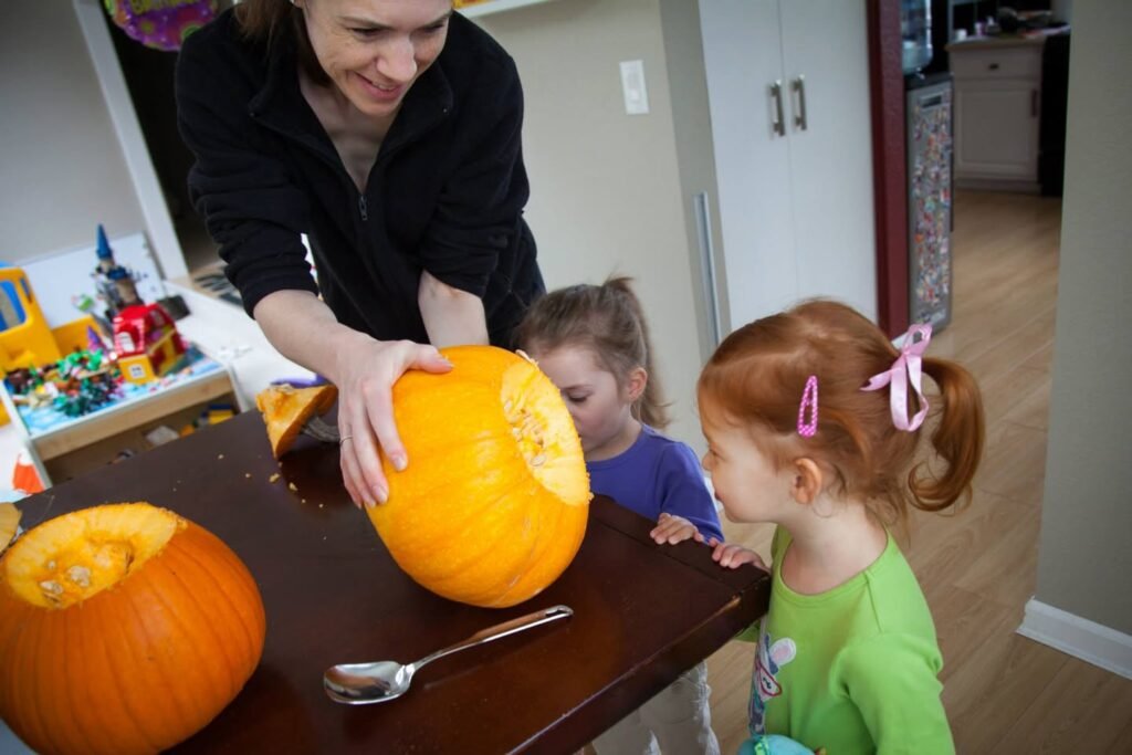 An adult helps children carve a pumpkin at a kitchen table.