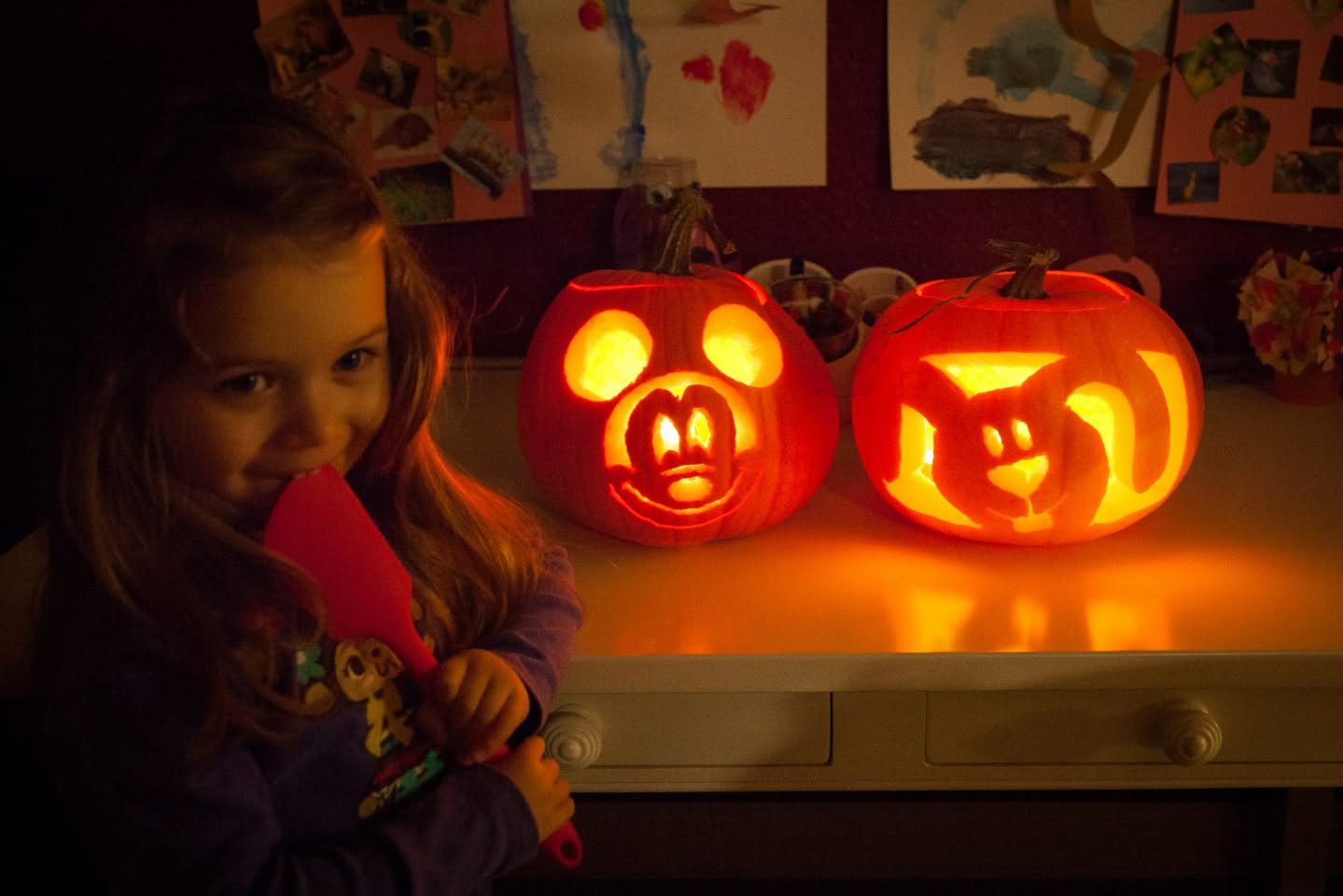 Pumpkins Three Ways A child smiles beside glowing carved pumpkins in a cozy, dimly lit room.