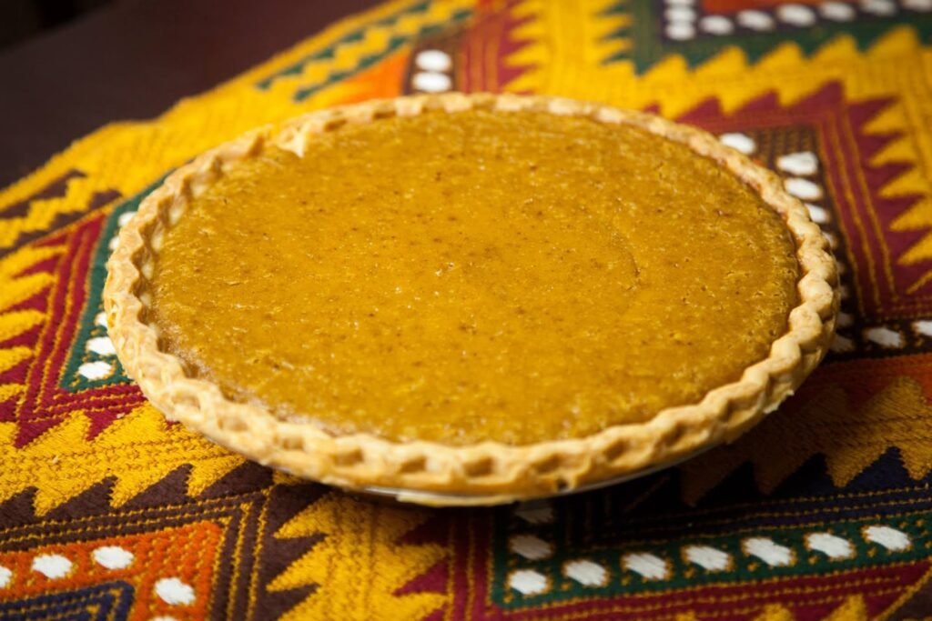 A closeup of a rustic fruit tart with a braided crust resting on a colorful patterned placemat.