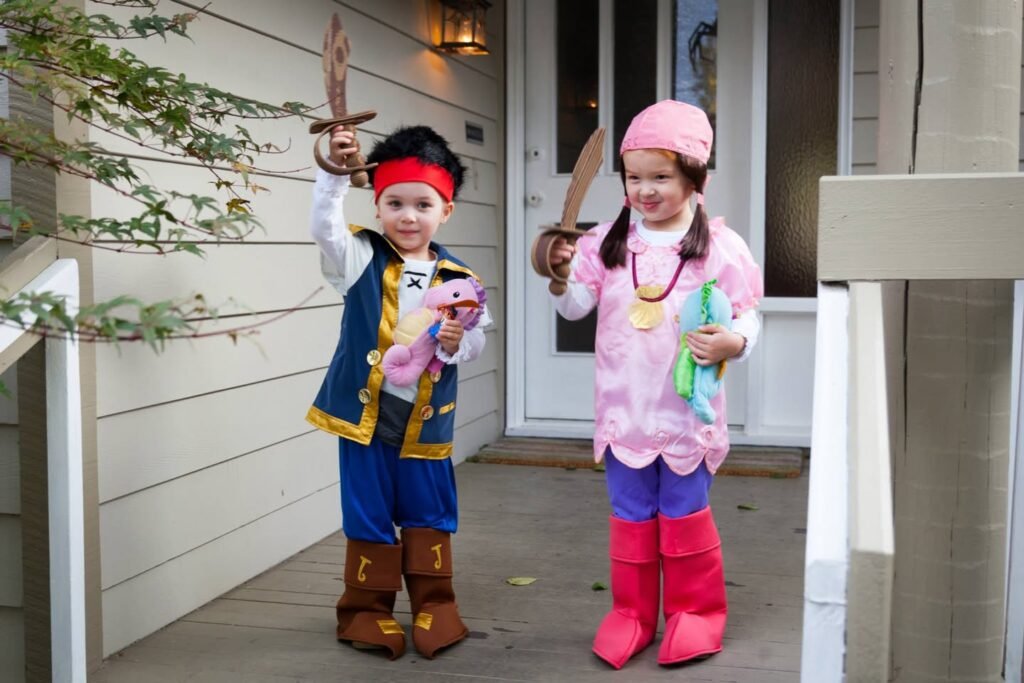 Two children dressed in matching Pinocchio and dinosaur costumes holding candy on a porch.