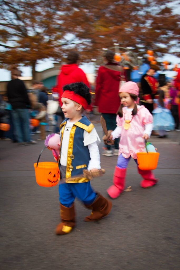 Two children in pirate and pink costumes walking together with orange pumpkin buckets.